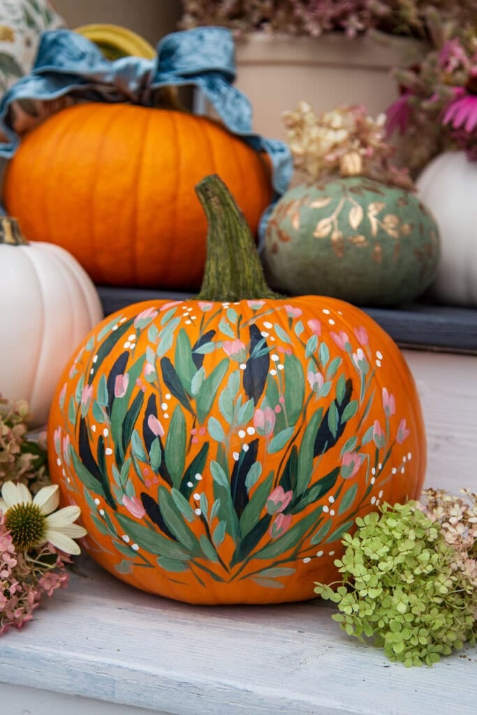 Hand-painted floral pumpkin with pink, green, and white leaves on an orange base.