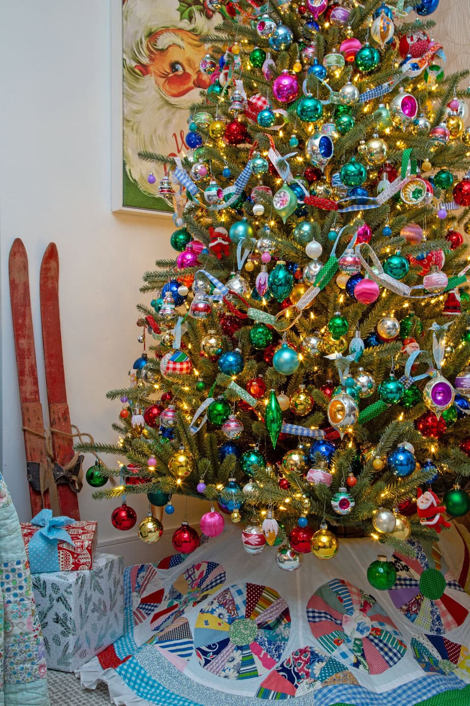 Colorful vintage Christmas tree packed with shiny bright ornaments and warm lights, styled with a patchwork tree skirt.