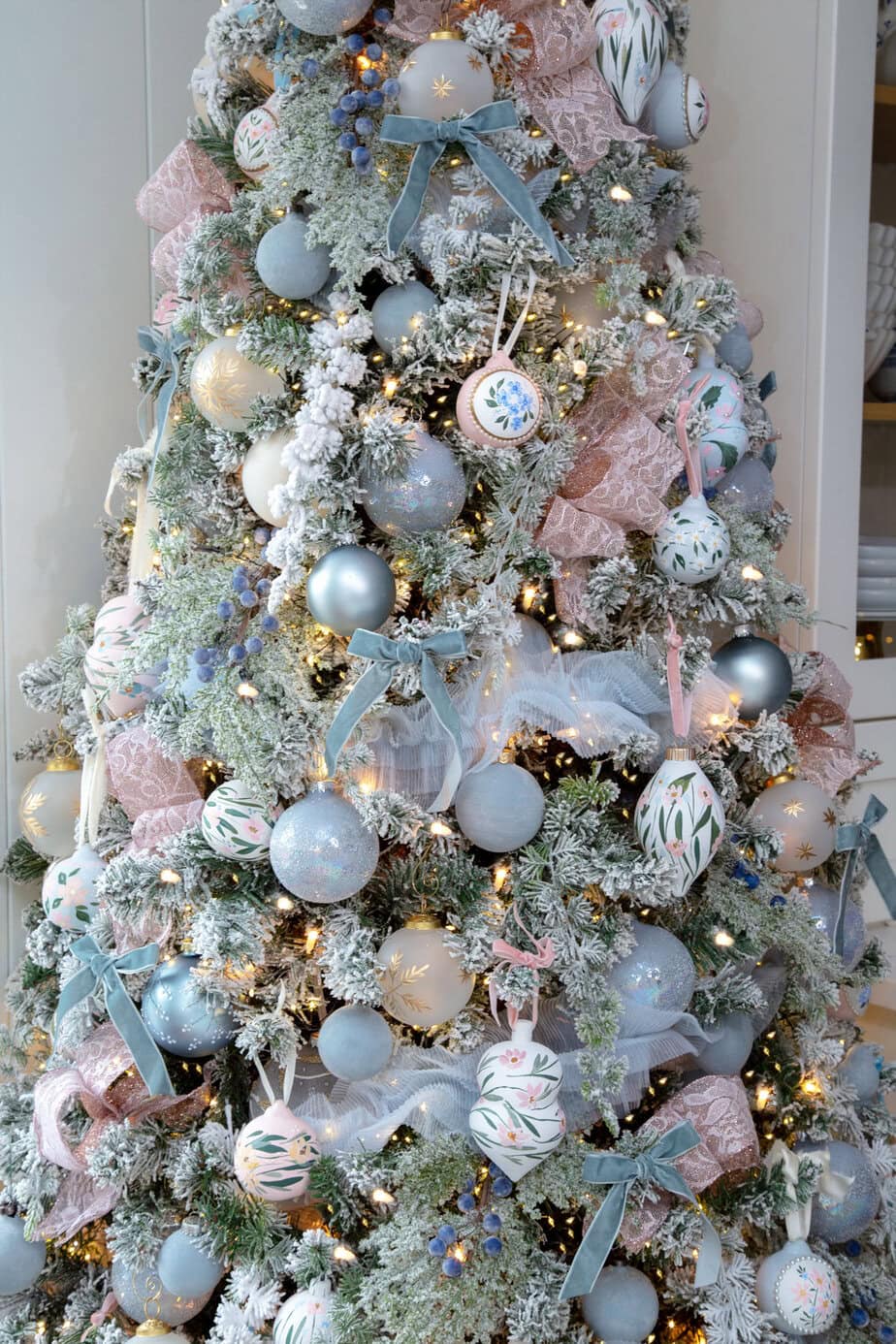 Flocked Christmas tree decorated in blush pink and soft blue with ribbon, velvet bows, and hand-painted ornaments.