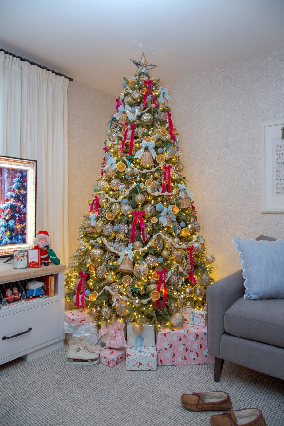 Vintage Christmas tree with gold ornaments, dried orange slices, and red and blue ribbon bows in a cozy living room.