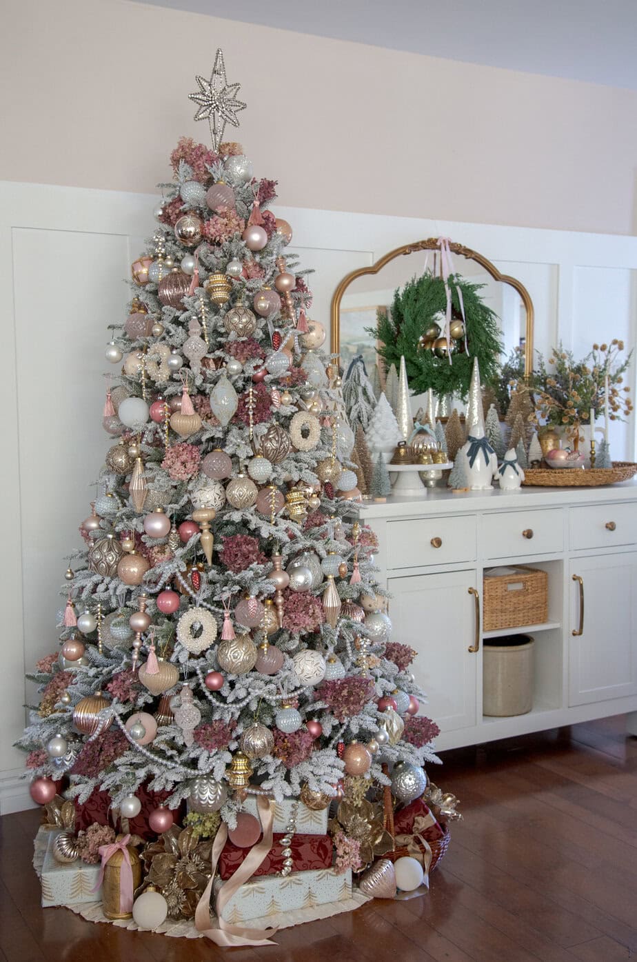 Pink and champagne Christmas tree with hydrangea picks, metallic ornaments, and warm lights in a cozy holiday corner.