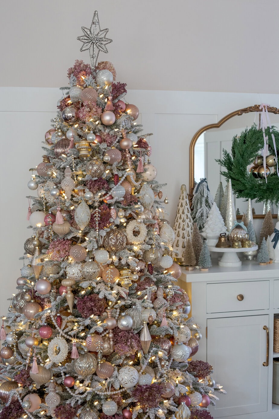 Pink and champagne Christmas tree with hydrangea picks, metallic ornaments, and warm lights in a cozy holiday corner.