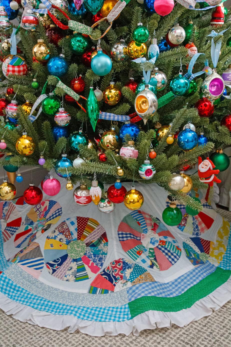 Colorful vintage Christmas tree packed with shiny bright ornaments and warm lights, styled with a patchwork tree skirt.
