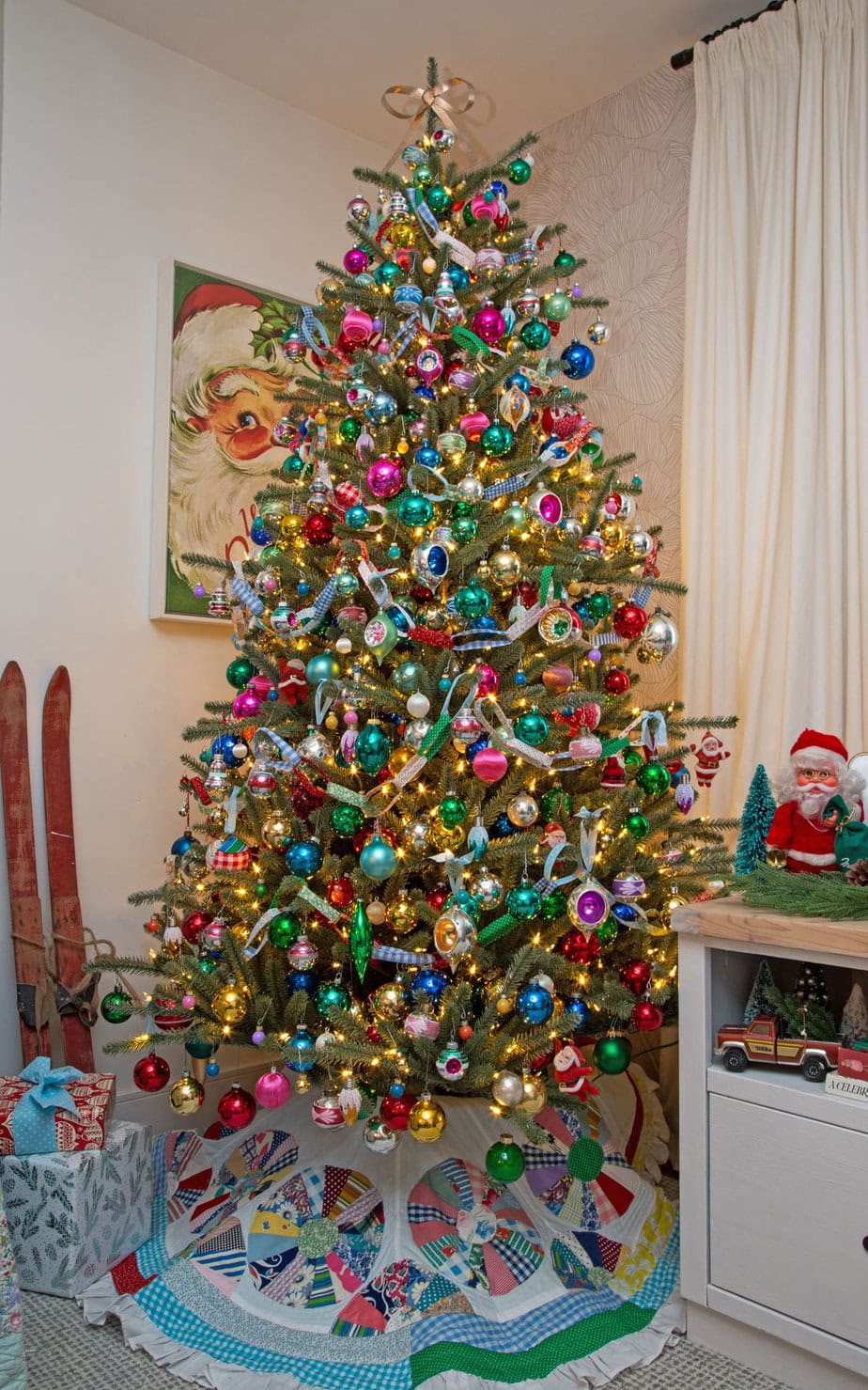 Colorful vintage Christmas tree packed with shiny bright ornaments and warm lights, styled with a patchwork tree skirt.