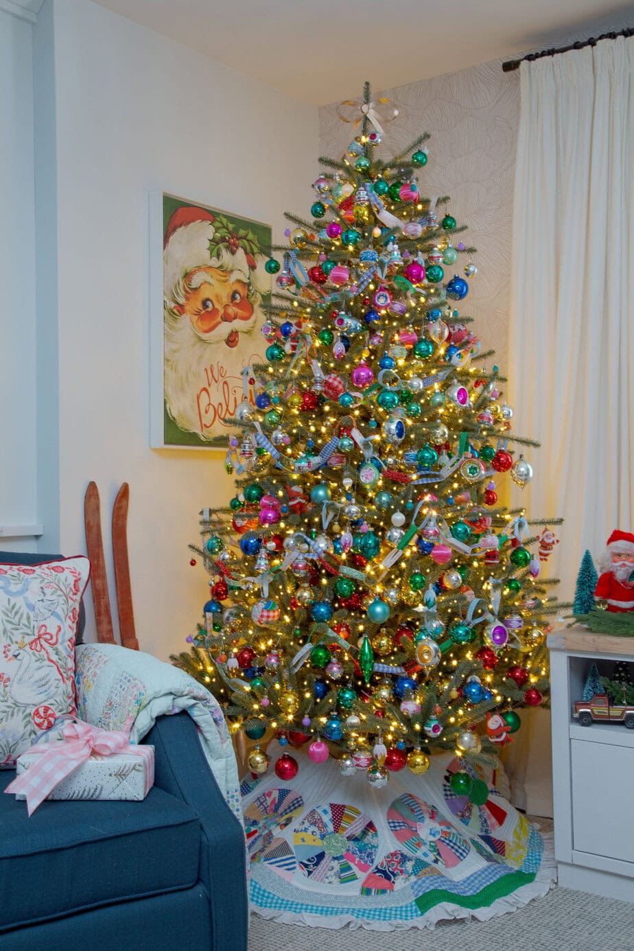Colorful vintage Christmas tree packed with shiny bright ornaments and warm lights, styled with a patchwork tree skirt.