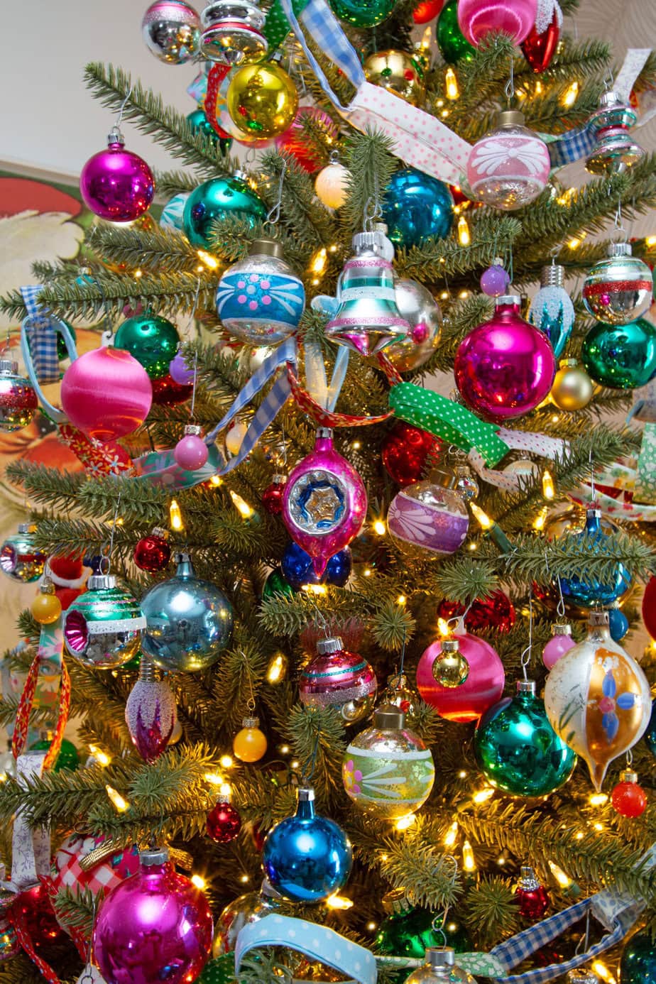 Colorful vintage Christmas tree packed with shiny bright ornaments and warm lights, styled with a patchwork tree skirt.