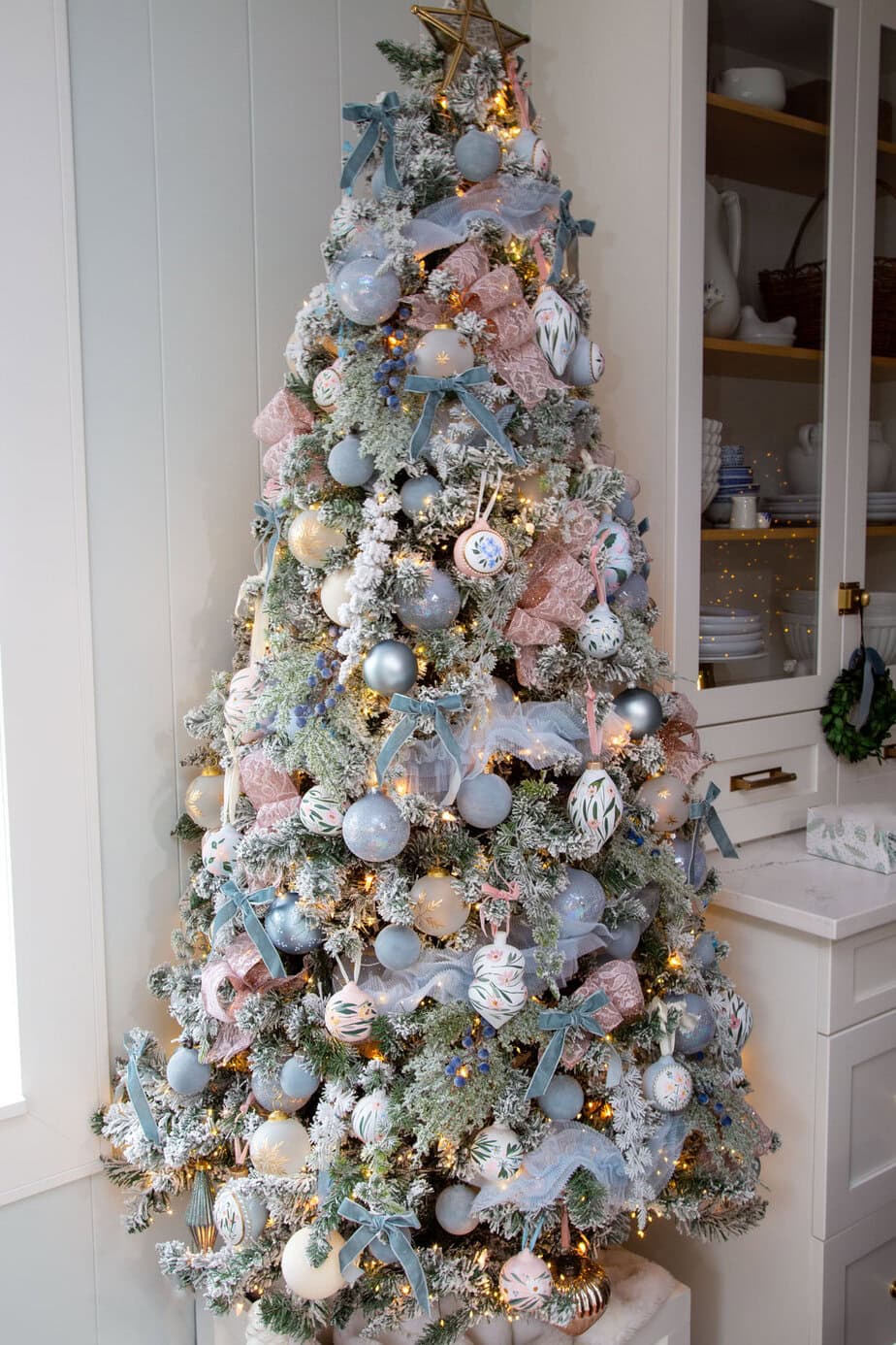 Flocked Christmas tree decorated in blush pink and soft blue with ribbon, velvet bows, and hand-painted ornaments.
